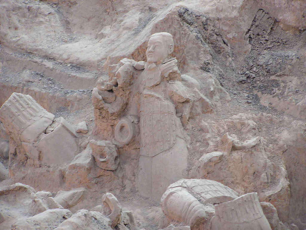 Partly excavated terracotta warrior lying in soil among clay fragments