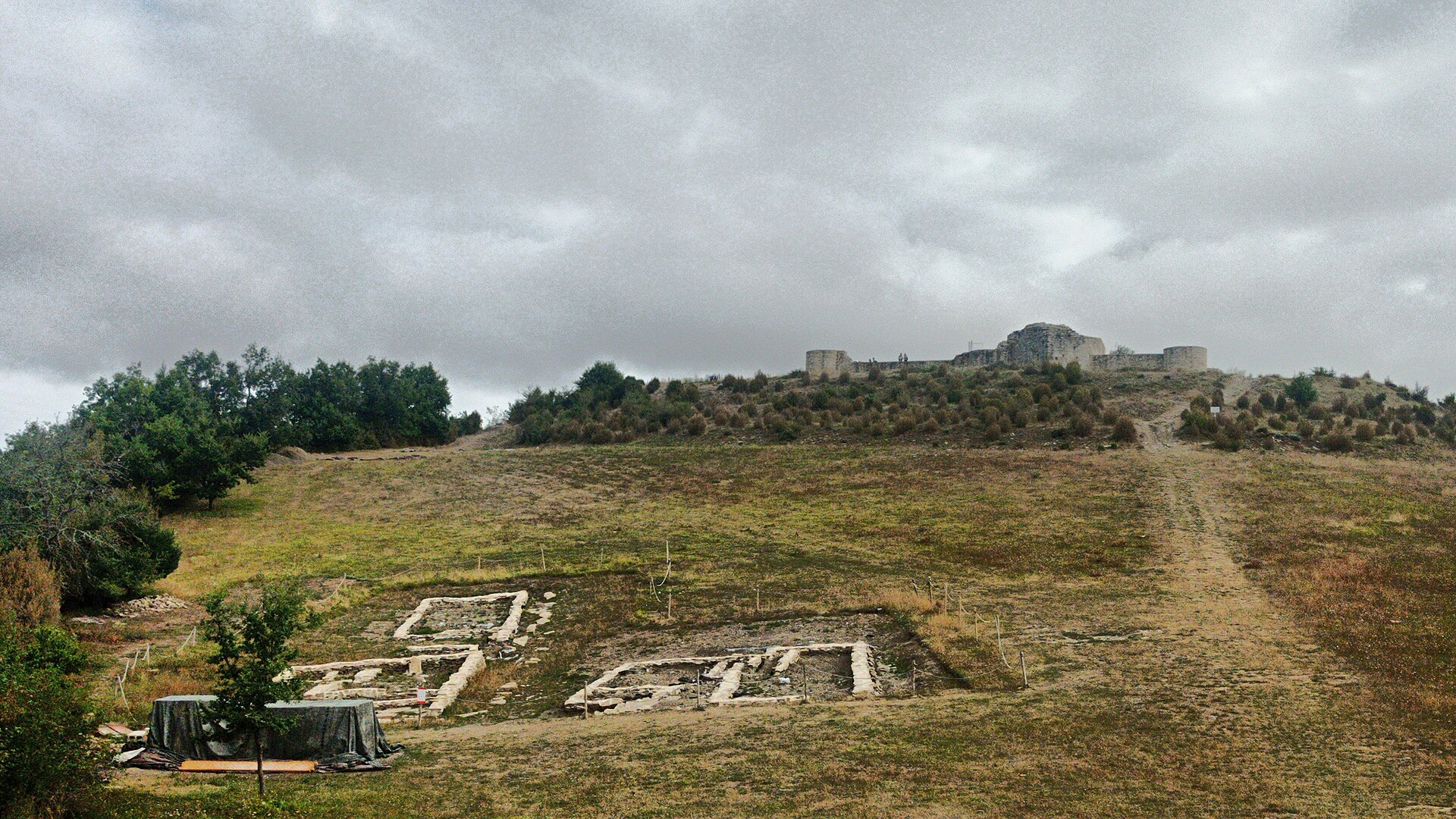 Excavated stone foundations of the hilltop village at Irulegi with castle ruins in view